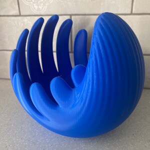 May include: A blue ceramic bowl with a unique hand-like design. The bowl has a textured surface and is perfect for holding fruit or other small items.