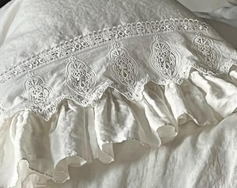 May include: White bedding set featuring a pillow with ornate lace trim and a ruffled edge. The bedspread has a matching ruffled skirt with tie closures. The overall aesthetic is soft and romantic, perfect for a bedroom.