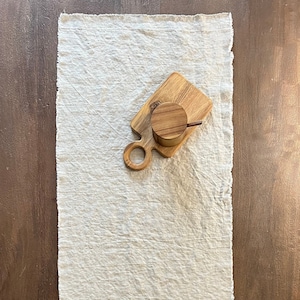 May include: A white linen table runner with a wooden chopping board and a glass cloche on top of a wooden base.