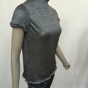 May include: A gray, short-sleeved, mock neck shirt with a slightly ruffled hem.