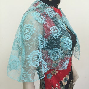 May include: A light blue lace shawl with a floral pattern. The shawl is draped over a mannequin wearing a black and red patterned shirt.