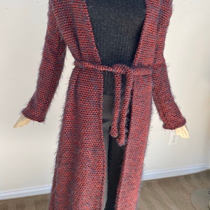 Puede incluir: Una larga chaqueta de punto con cinturón de lazo. La chaqueta es una mezcla de gris oscuro y naranja.