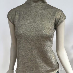 May include: A gold metallic short-sleeved turtleneck top with a slightly ruffled hem.