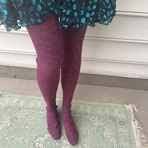 May include: A pair of burgundy ribbed tights with a textured knit pattern. The tights are worn with a short, teal skirt with a floral pattern.