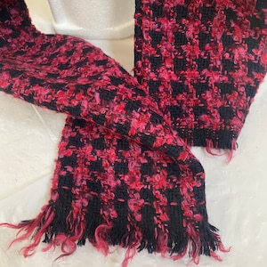 May include: A black and pink scarf with a textured, fuzzy design and frayed edges.