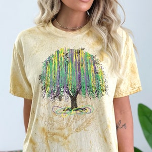 May include: A yellow tie-dye t-shirt with a green, purple, and gold tree design. The tree is made of beads and is reminiscent of Mardi Gras.