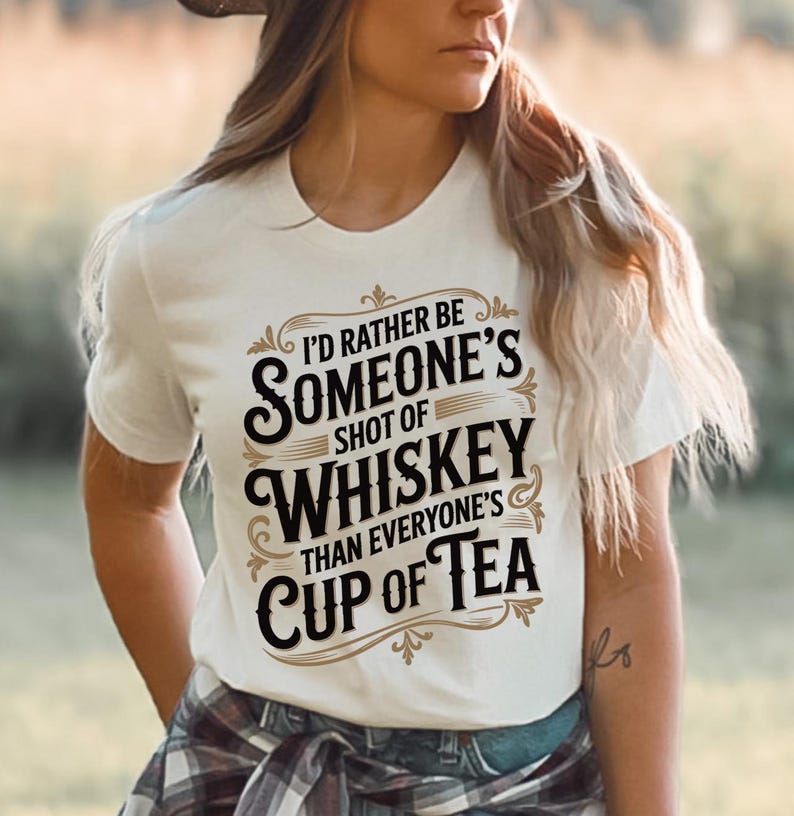 May include: White t-shirt with the text "I'd rather be someone's shot of whiskey than everyone's cup of tea" in a decorative font. The shirt is short-sleeved and has a crew neck.
