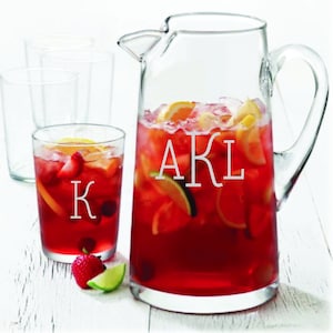 May include: A clear glass pitcher and tumbler filled with red sangria, garnished with fruit. The pitcher and tumbler are engraved with the initials "AKL" and "K" respectively.