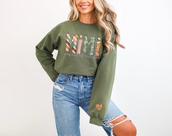 May include: A green sweatshirt with the text "The Mimi" in colorful patterned letters. The text "every memory is a story" is written below the main text.