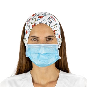May include: A woman wearing a white medical scrub top and a blue surgical mask. She is also wearing a white headband with a colorful pattern of medical symbols, including hearts, pills, and crosses.