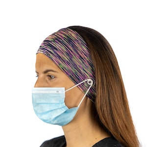 May include: A woman wearing a blue surgical mask with a headband that has a button to hold the mask straps. The headband is a multi-colored pattern of pink, purple, green, and black.