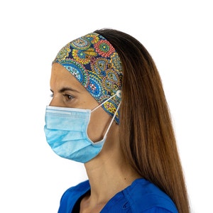 May include: A woman wearing a blue surgical scrub top and a blue and pink patterned headband with buttons to hold a face mask. The headband has a paisley design.