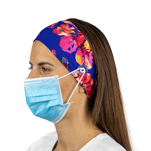 May include: A woman wearing a blue headband with a floral print and a light blue face mask. The headband has a clear plastic button on the side to hold the mask straps.