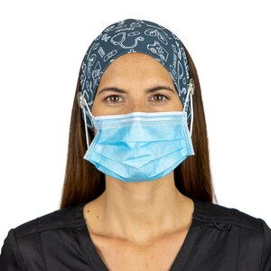 May include: A woman wearing a blue and white patterned headband with a light blue surgical mask. The headband has a white elastic strap that goes around the ears. The woman is wearing a dark grey scrub top.