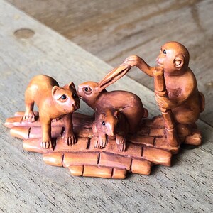 Pode incluir: Uma escultura de madeira esculpida à mão de um macaco, um coelho, um gato e um pequeno roedor. Os animais estão em pé numa plataforma feita de bambu esculpido.