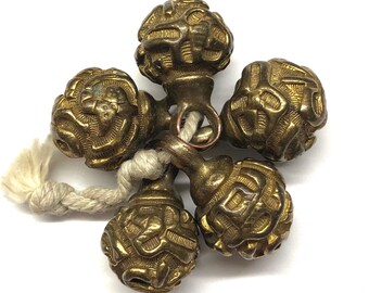 May include: Five gold-colored metal beads with intricate designs, connected by a white cord. The beads are round and have a textured surface.