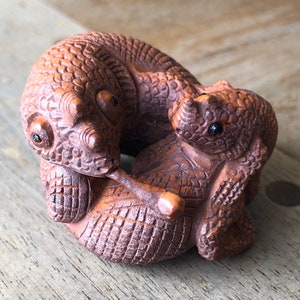 Könnte beinhalten: Eine handgeschnitzte Holzskulptur von zwei ineinander verschlungenen Eidechsen mit detaillierten Schuppen und schwarzen Augen.