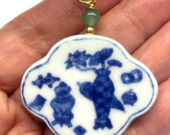 May include: A blue and white porcelain pendant with a floral design and a bird. The pendant is attached to a green cord with a gold bead.