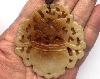 Op de afbeelding: Een gegraveerde jade hanger met een bloemmotief, in een bruin en wit kleurenschema. De hanger is bevestigd aan een bruin koord met een koraal kralen.