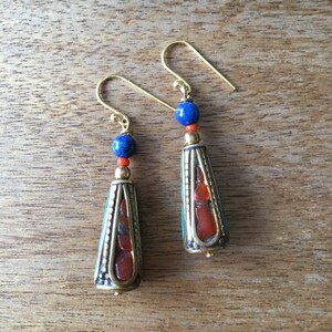 May include: A pair of gold dangle earrings with a blue and orange stone design. The earrings feature a cone-shaped bead with a gold trim and a blue stone at the top.