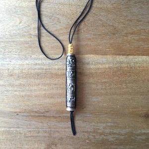 May include: A silver prayer wheel with intricate carvings and a black cord. The prayer wheel is suspended from a black cord and has a yellow tassel.