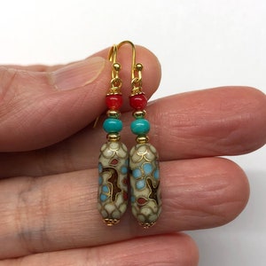 May include: A pair of gold dangle earrings with a white, blue, and red patterned bead, a turquoise bead, and a red bead on each earring.