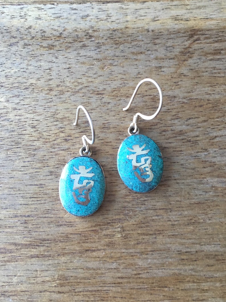 May include: A pair of silver earrings with turquoise blue oval-shaped charms. Each charm has a silver Chinese character etched into the surface.