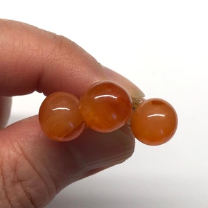 May include: Three round, orange carnelian beads strung together on a gold wire.