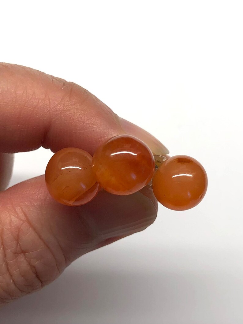 May include: Three round, orange carnelian beads strung together on a gold wire.