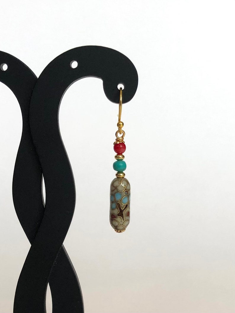 May include: Gold dangle earrings with a turquoise, red, and gold bead cluster and a patterned cylinder bead.