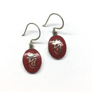 May include: A pair of silver earrings with red oval-shaped charms. Each charm features a silver Chinese character on a red background.