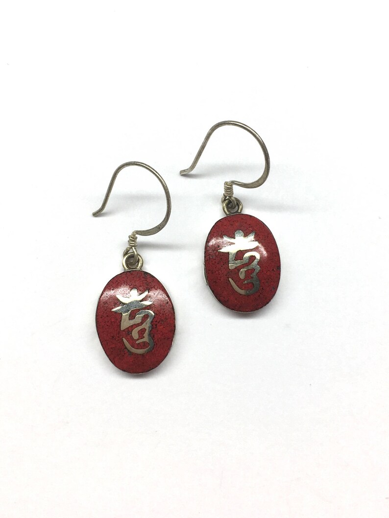 May include: A pair of silver earrings with red oval-shaped charms. Each charm features a silver Chinese character on a red background.