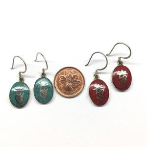 May include: Four silver earrings with oval-shaped charms. Two charms are turquoise blue with silver lettering and two charms are red with silver lettering.