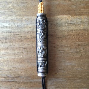 May include: A silver prayer wheel with intricate carvings and a black cord with yellow accents.
