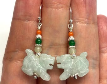 May include: A pair of jade green dangle earrings featuring a carved jade lion charm, green and orange beads, and silver hooks.