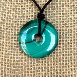 May include: A green malachite stone pendant in the shape of a donut, hanging from a black cord necklace.