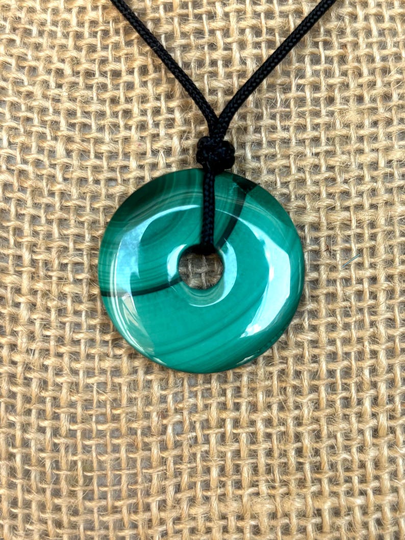 May include: A green malachite stone pendant in the shape of a donut, hanging from a black cord necklace.