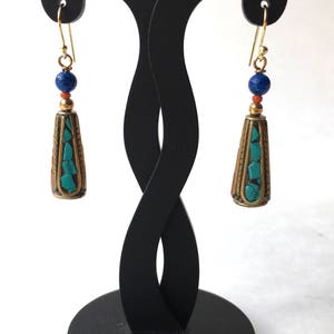 May include: A pair of gold tone earrings with turquoise and lapis lazuli beads. The earrings are hanging from a black earring stand.