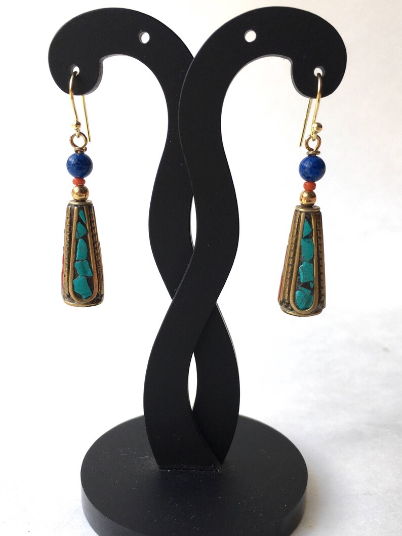 May include: A pair of gold tone earrings with turquoise and lapis lazuli beads. The earrings are hanging from a black earring stand.