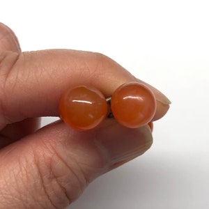 May include: A pair of orange carnelian gemstone earrings. The earrings are round and have a smooth, polished finish.