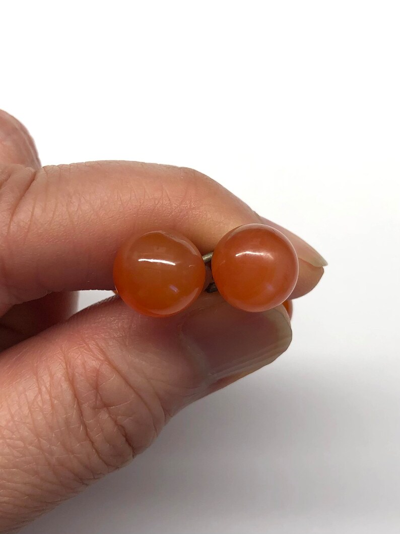 May include: A pair of orange carnelian gemstone earrings. The earrings are round and have a smooth, polished finish.