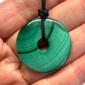 May include: A green malachite stone pendant in the shape of a donut, with a black cord.