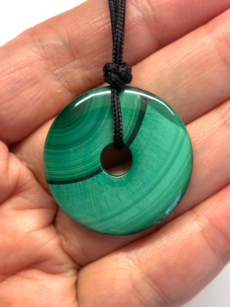 May include: A green malachite stone pendant in the shape of a donut, with a black cord.