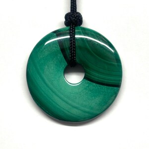 May include: A green malachite stone pendant in the shape of a donut, with a black cord.