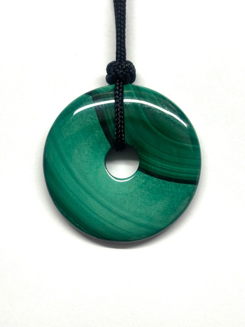 May include: A green malachite stone pendant in the shape of a donut, with a black cord.