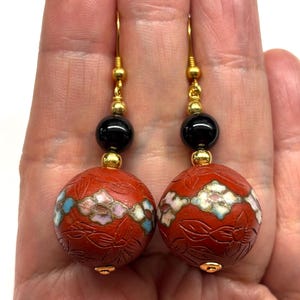 May include: A pair of dangle earrings with red, white, and blue floral enamel beads, black onyx beads, and gold accents.