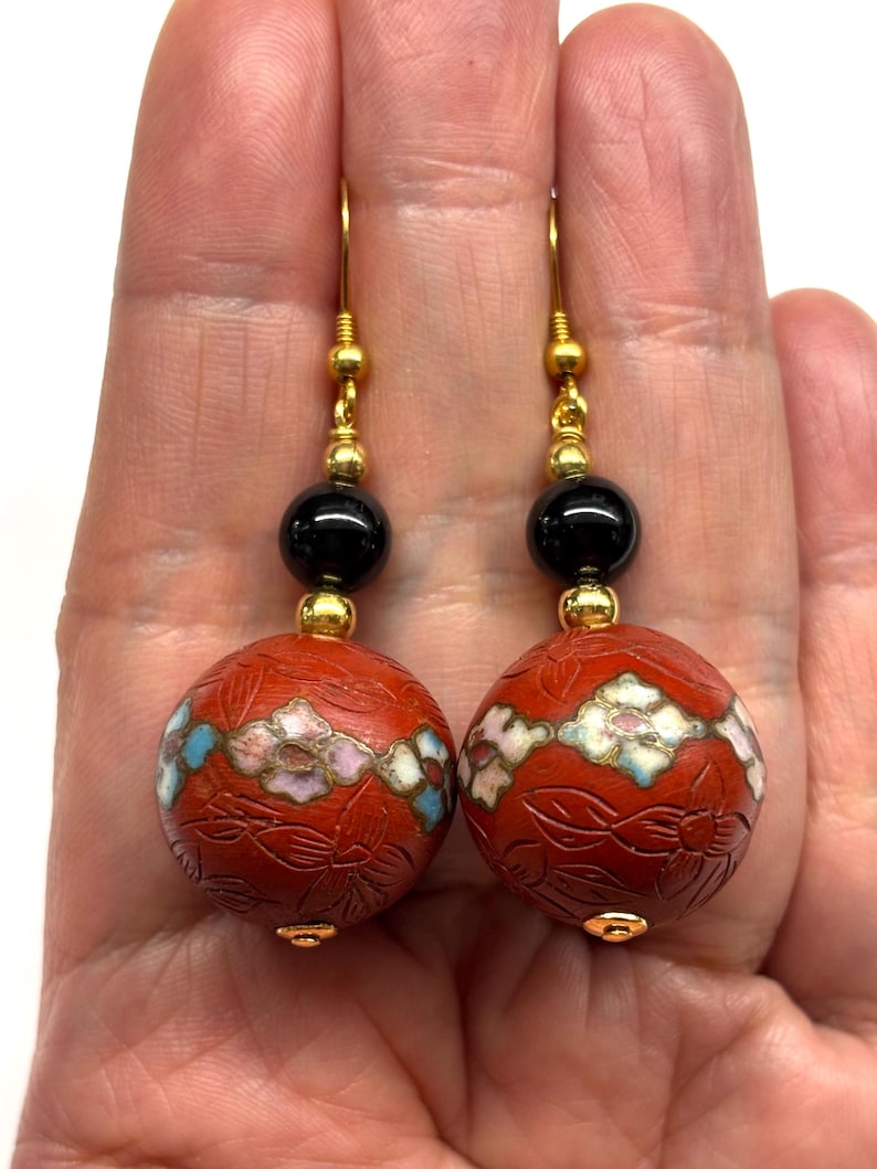 May include: A pair of dangle earrings with red, white, and blue floral enamel beads, black onyx beads, and gold accents.
