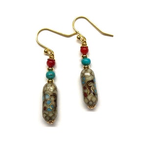 May include: A pair of gold dangle earrings with a white, blue, and red enamel bead. The bead has a floral pattern.
