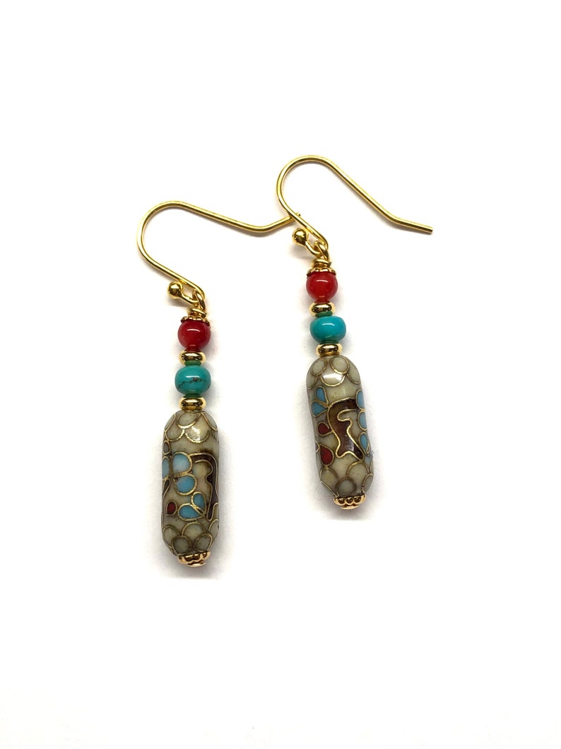 May include: A pair of gold dangle earrings with a white, blue, and red enamel bead. The bead has a floral pattern.