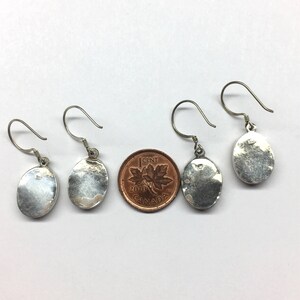 May include: Three pairs of silver oval earrings with a hook closure. The earrings are about the size of a Canadian penny.